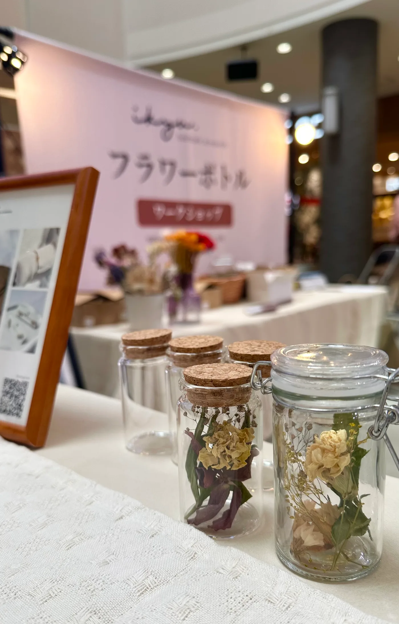 ikyuのフラワーボトルワークショップのブース。桜色のバナーの前に、ドライフラワーを詰めた小さなガラスボトルが並ぶ