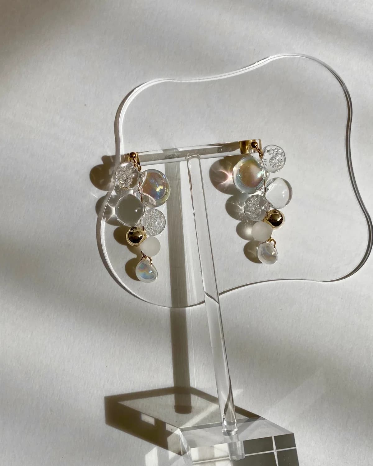 波形のアクリルスタンドに揺れるsoap bubble。しゃぼん玉のような虹色の透明ビーズに、窓の光と影が差す