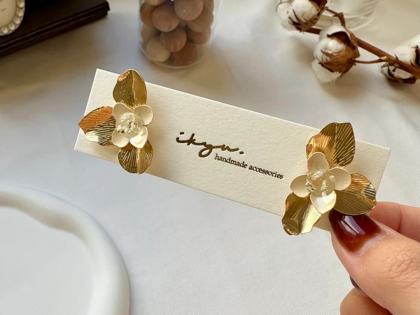 金の花のピアスを留めたブランドカードを、お客様へ手渡すように掲げた作り手の手元